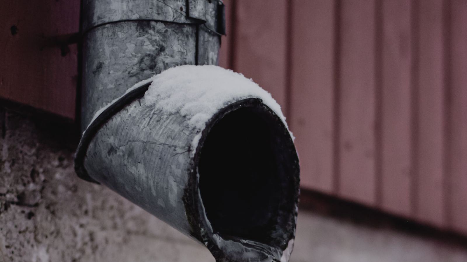 Frozen outdoor pipe with a thick icicle after a hard freeze — protect plumbing before freezing nights arrive