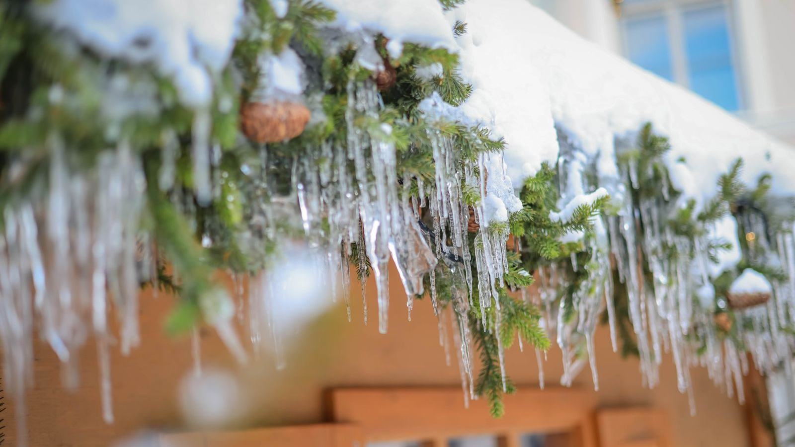 Icicles forming along a snowy roof edge — an early warning sign of ice dams backing water under the shingles