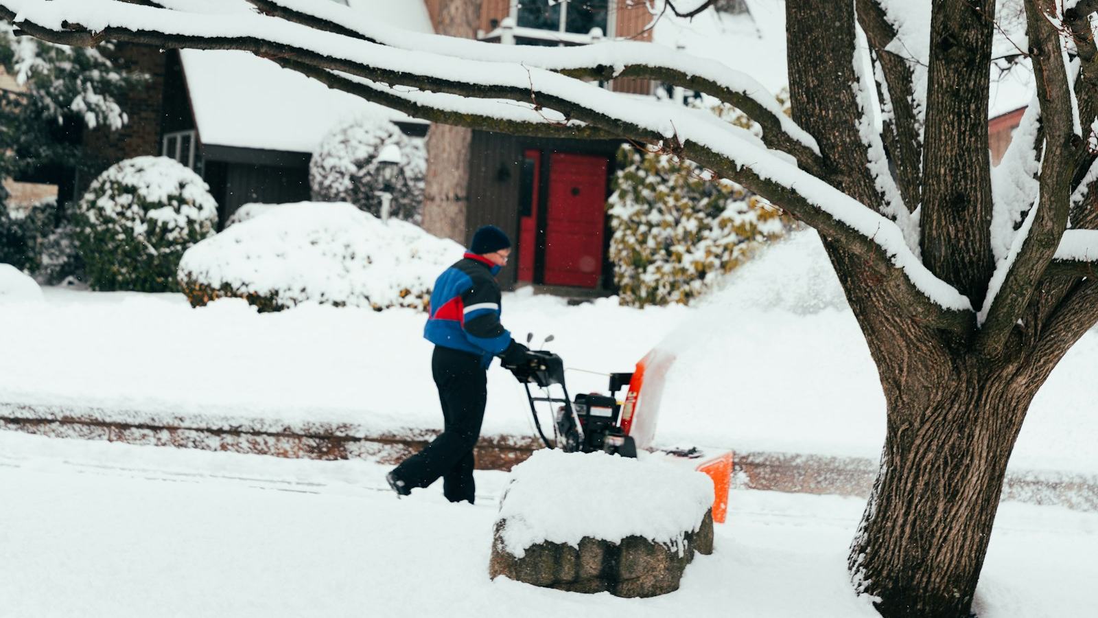 Homeowner clearing a snowy driveway with a two-stage snow blower after the first plowable snowfall