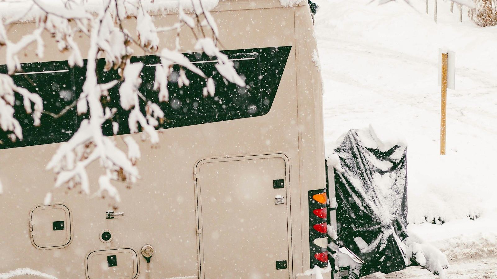 Motorhome parked on a snowy street in falling snow — drain and antifreeze the water system before the first hard freeze
